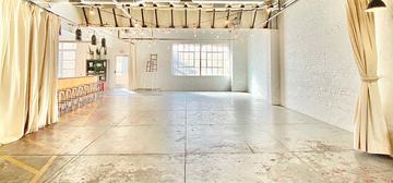 Open warehouse event space at The Venue at Plenty with concrete floors, exposed wood beams, string lights, and white brick walls in downtown Oklahoma City