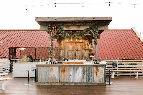 Rustic wooden bar with corrugated metal paneling and a greenery arch on the rooftop at The Venue at Plenty in Oklahoma City